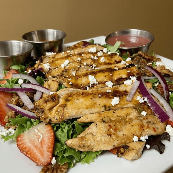 Grilled chicken salad with strawberries, red onion, feta, candied pecans, and two dressing cups.