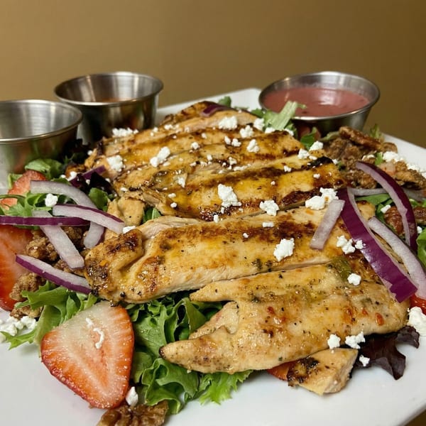 Grilled chicken salad with strawberries, red onion, pecans, feta cheese, and two dressing cups.