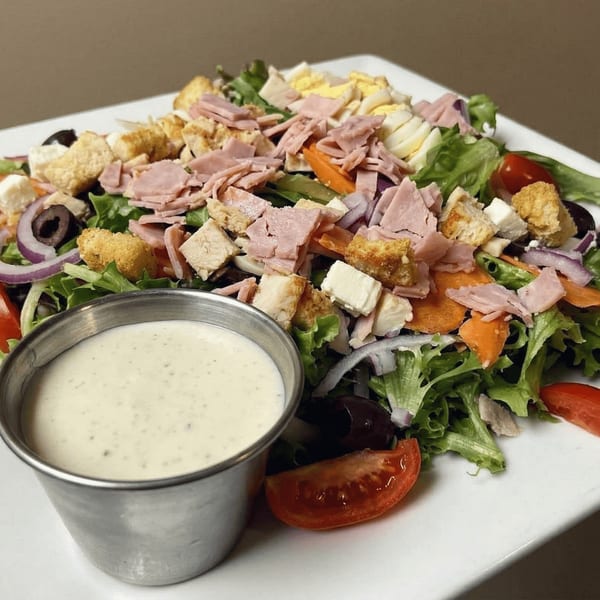 A vibrant chef salad with ham, hard-boiled eggs, croutons, and vegetables, served with a side of dressing.