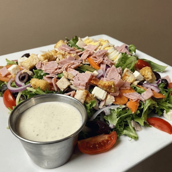 A vibrant chef salad with ham, hard-boiled eggs, croutons, and a side of ranch dressing.